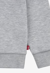 Gros plan sur les poignets d'un sweat-shirt gris avec un ourlet côtelé et une petite étiquette en tissu rouge Levi's sur la couture latérale.