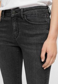 Jeans negros ajustados con una textura suave y sutiles desgastes, que cuentan con bolsillos frontales y un cierre de botón en la cintura.