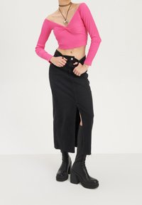 Rosa ribbad crop top med långa ärmar och tvistdesign, tillsammans med en svart denimkjol med en sidoklyvning och knähöga svarta klackstövlar.