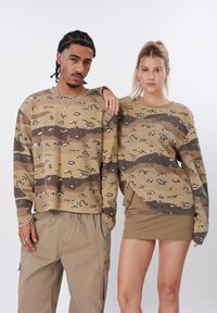 Μακριά μπλουζάκια με μοτίβο καμουφλάζ, υφασμένα από υφή, φορεμένα με μπεζ παντελόνια cargo και μια αντίστοιχη μίνι φούστα.