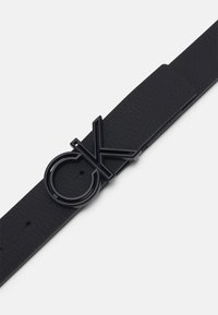 Cintura in pelle nera con finitura testurizzata, dotata di una fibbia opaca nera con il logo "CK". Design semplice, con più fori di regolazione.