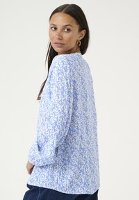 Blouse à manches longues bleu clair avec un motif abstrait blanc, dotée d'un col rond et d'une coupe décontractée, fabriquée en tissu léger.