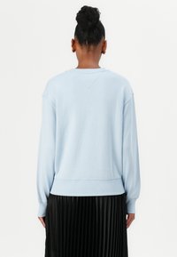 Light blue sweatshirt in a relaxed fit with long sleeves. Features ribbed cuffs and hem, with a V-shaped seam at the back. Paired with a black pleated skirt.