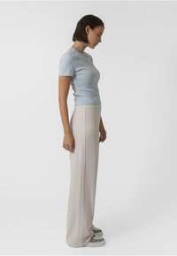 Haut bleu clair à manches courtes à côtes associé à un pantalon large crème et des baskets à motifs, vu de côté sur fond blanc.