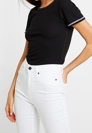 Black ribbed short-sleeve top with a round neck and white accents, paired with white fitted jeans featuring a front button and pockets.