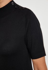 Pulover negru cu mânecă scurtă, guler înalt și accente cu nasturi pe umărul stâng. Materialul are o textură netedă și un design ajustat.