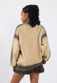 Overmaat beige sweatshirt met een donkere ombre-gradiënt, zachte stof, geribde manchetten, ronde halslijn, gecombineerd met een donkere, versleten mini-jurk.