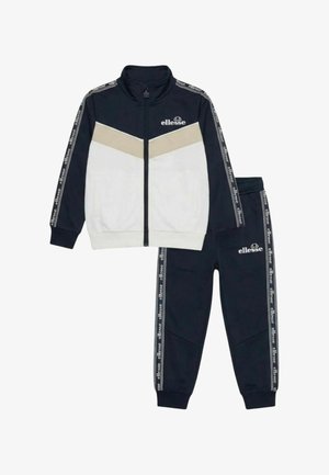 Veste zippée bleu marine et blanche avec chevron beige, pantalon assorti bleu marine, les deux arborant le logo ellesse et des détails de bande de marque.