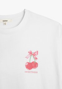 Witte katoenen t-shirt met een grafisch ontwerp van twee roze kersen met een strik en het woord "SWEETNESS" in roze tekst onder het ontwerp.
