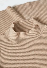 Pull à col roulé beige côtelé avec un col haut. Le tissu présente des lignes verticales, créant un aspect texturé.