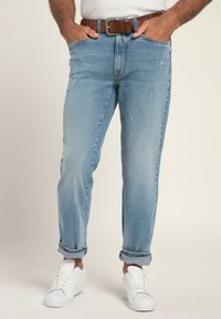 Jeans de mezclilla azul claro con un corte recto, que presentan un desgaste sutil, dobladillos enrollados y un cinturón marrón. Combinados con zapatillas blancas.