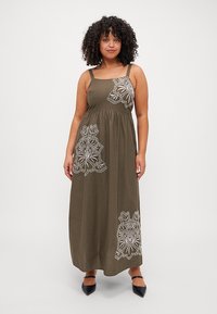 Robe maxi vert olive avec broderies blanches ressemblant à de la dentelle sur le devant. Elle possède de fines bretelles et un corsage ajusté avec une jupe fluide.