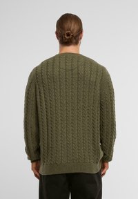 Zielona oliwkowa sweterek dzianinowy z fakturowanym wzorem w warkocz, okrągłym dekoltem oraz ściągaczami przy mankietach i u dołu. Luźny krój z opadającymi szwami ramion.