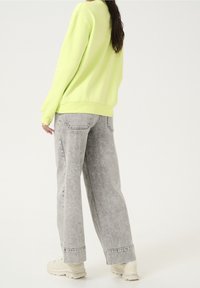 Neon zielona bluza z prążkowanymi mankietami, w połączeniu z jasnoszarymi, szerokimi spodniami dżinsowymi o wyblakłej fakturze i surowych krawędziach. Neutralne trampki.