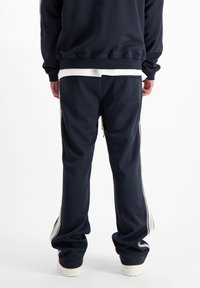 Marineblauwe trainingsbroek met witte zijstrepen, elastische tailleband en een achterzak. Gemaakt van een gladde stof met een relaxte pasvorm.
