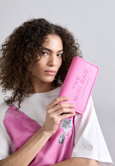 Roze leren portemonnee met reliëftekst "THE MINI BAG" van Marc Jacobs, met een gladde textuur en ritssluiting, tegen een lichte achtergrond gehouden.