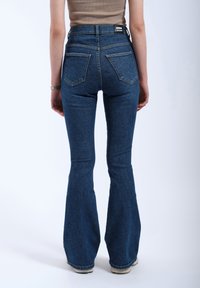 Dark blue flared jeans with a high waist, featuring a seamless back, two rear pockets, and a woven label at the back waistband.