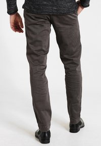 Pantalon en coton gris avec une coupe slim, une texture subtile et des jambes droites. Fini avec une taille mi-haute et porté avec des chaussures noires.