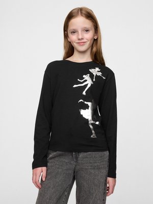 Chemise noire à manches longues avec des graphiques de danseur en argent. Tissu doux, coupe décontractée avec un col rond, portée avec un pantalon gris.