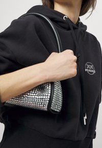 Svart handväska med silverfärgade rhinestones, triangulär form, texturerad yta, läderdetaljer, bärs med en hand, matchad med en svart hoodie.