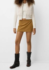 Vit ribbad sweaterväst med konstpäls, tanfärgad minikjol och svarta läderankelstövlar med metalldetaljer. Enkel, modern design.