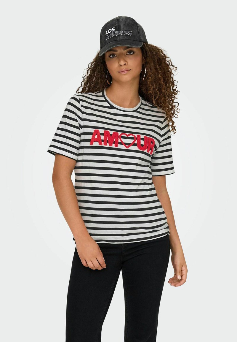 Gestreepte ronde hals T-shirt in grijs en zwart met een gestructureerde rode "AMOUR" graphic; gecombineerd met zwarte jeans en een zwarte pet met "LOS ANGELES" tekst.