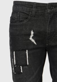 Blugi din denim negru cu zone uzate și accente de cusături albe, prevăzuți cu un buzunar pe șold și închidere cu nasture.