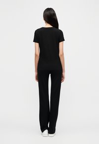 Μαύρο μακό μπλουζάκι με κοντά μανίκια σε συνδυασμό με μαύρο παντελόνι φαρδύ στο κάτω μέρος, και τα δύο κατασκευασμένα από απαλό, λείο ύφασμα. Απλός σχεδιασμός χωρίς σχέδια ή διακοσμητικά στοιχεία.