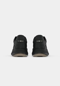Zapatillas deportivas negras con una parte superior suave, puntera redondeada y suela texturizada, que presentan acentos minimalistas en el talón.