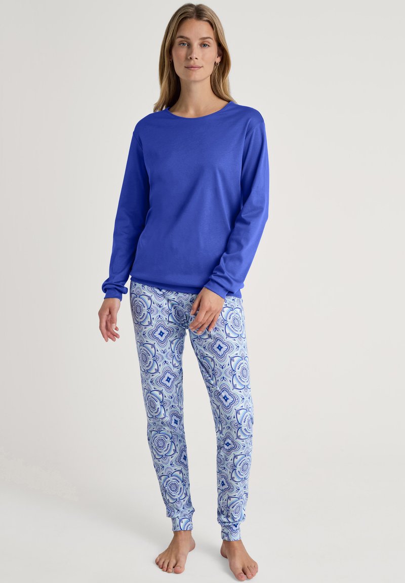 Maglietta blu a maniche lunghe con scollo rotondo abbinata a pantaloni da pigiama bianchi e blu con motivi intricati e polsini alla caviglia.