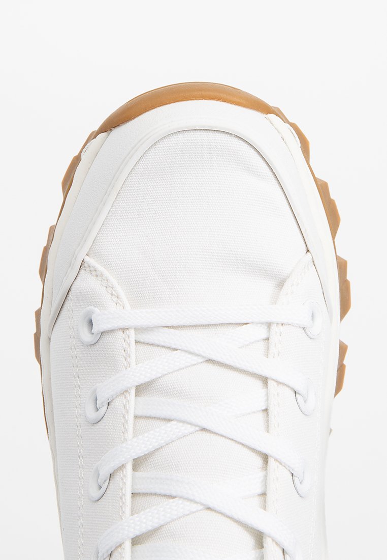 Sneaker bianco in tela con parte superiore testurizzata, suola in gomma e soletta color beige. Caratterizzato da sei occhielli bianchi e lacci piatti bianchi per la chiusura.