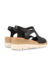 Sandalias de cuero negro con un diseño recortado, correa tipo slingback y suela cuña en crema y marrón claro, con tacones de goma texturizada.