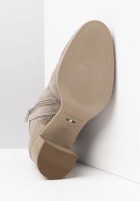 Beige Wildleder-Ankle Boot mit einem strukturierten seitlichen Reißverschluss und gemusterten Details, einer glatten Gummisohle und einem geprägten Markennamen an der Unterseite.