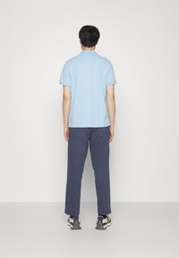 Ljusblå kortärmad polo med mörkblå byxor. Modell vänd bort, iförd grå och marinblå sneakers.