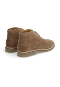 Bottines en daim marron à bout rond, avec un laçage à deux œillets et une semelle en caoutchouc texturée. Elles comportent une bande beige cousue et un marquage discret.