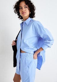 Chemise oversize bleu clair avec un col pointu, fermeture à boutons et manches retroussées, associée à un short assorti avec une taille élastique et des poches.