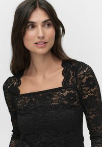 Zwarte kanten top met een vierkante halslijn en lange mouwen, voorzien van een getextureerd bloemenpatroon en golvende randen bij de halslijn.