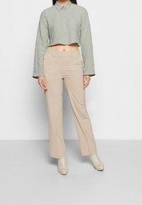 Camisa corta de color verde claro, texturizada, con mangas largas y cierre de botones, combinada con pantalones rectos beige y botas de tobillo color crema.