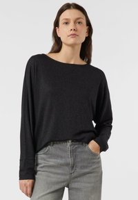 Czarna bluzka z długim rękawem i dekoltem typu łódka, wykonana z teksturowanej, lekko połyskującej tkaniny. W połączeniu z szarymi, wysokim stanem dżinsami.