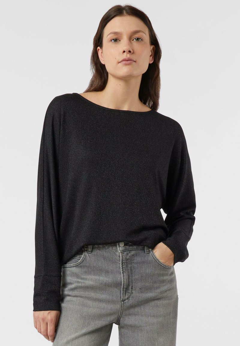 Czarna bluzka z długim rękawem i dekoltem typu łódka, wykonana z teksturowanej, lekko połyskującej tkaniny. W połączeniu z szarymi, wysokim stanem dżinsami.