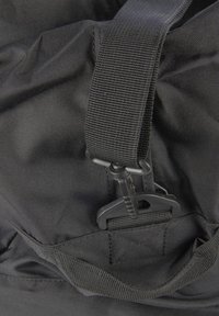Close-up van een zwarte stoffen rugzak, met een gestructureerde buitenkant, verstelbare webbing schouderband en plastic sluiting. 
