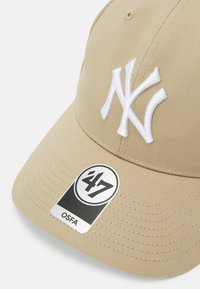 Beige cap with a white embroidered "NY" logo, featuring a curved brim and a tag showing "47" and "OSFA" on a smooth textured fabric.