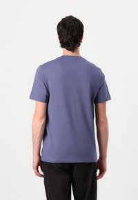 T-shirt med kort ärm och rund halsringning i ensfärgad ljuslila tyg, med en avslappnad passform och mjuk textur, bärs med mörka byxor.