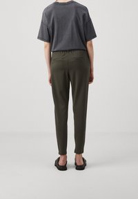 Grijze oversized t-shirt met korte mouwen, gecombineerd met olijfgroene, taps toelopende broek met een elastische tailleband en twee achterzakken. Zwarte sandalen.