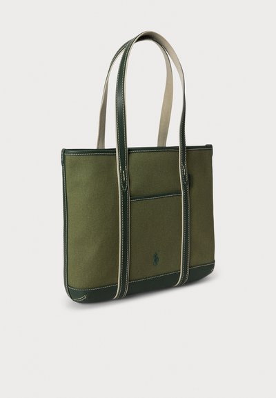 Grønn lerretstoteveske med mørkegrønne lærdetaljer, to lange håndtak, en frontlomme og kontrastsydd detalj.