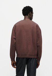 Καφέ βαμβακερό φούτερ με στρογγυλή λαιμόκοψη, χαλαρούς ώμους και ριμπ μανσέτες. Διαθέτει άνετη εφαρμογή και απαλή υφή.