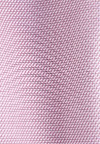 Gros plan d’un tissu avec un motif chevrons rose et blanc créant un design texturé et géométrique.