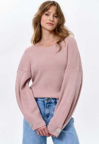 Hellrosa geripptes Sweatshirt mit weiten Ärmeln und Knopfakzenten, kombiniert mit hellblauen Jeans. Glatte Textur und lockere Passform.