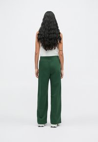 Pantalons de survêtement larges verts avec une taille à cordon de serrage, en matériau doux, associés à un débardeur blanc ajusté, vus de l'arrière.