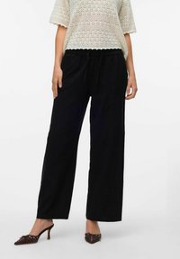Pantalons larges noirs avec une taille élastique et un cordon de serrage. Composés d'un tissu léger, présentant une silhouette décontractée.